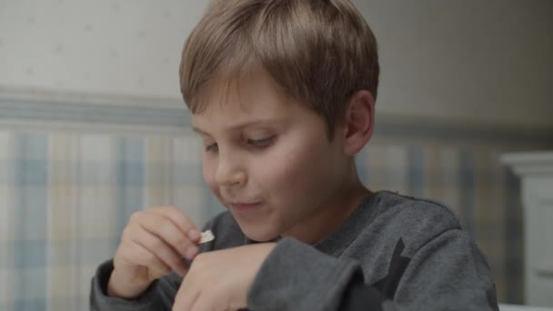 Criança autista comendo lanches saudáveis em câmera lenta sentada à mesa. O rapaz está feliz com a comida. Consciência do autismo — Vídeo de Stock