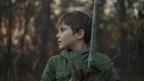 Middle plan of boy grimacing and holding dry tree branches in his hands in fall forest on sunset in slow motion. — Stock Video
