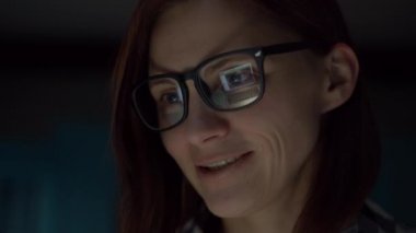 30 'lu yaşlarda, gözlüklü, gülümseyen bir kadının gece geç saatlerde evdeki erkek arkadaşıyla internette konuştuğu görüntüleri. Kadın gözlüklerinde konuşan adamla bilgisayar ekranı. 
