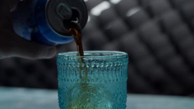 Mavi kola kutusunu kapat ve buzla dolu mavi bardağa kola dök. Mavi bardakta köpüklü kola, yavaş çekimde yakın çekim. 