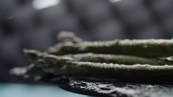 Close up of rotating fresh asparagus stalks bunch laying on black dish, slow motion macro view. — Stock Video