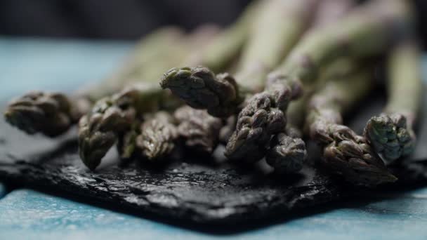 Gros plan de bouquet d'asperges fraîches posées sur un plat noir, éclaboussures d'eau au ralenti macro vue . — Video