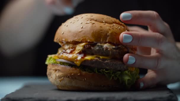 Ženské ruce krájející mňamkový burger s dvojitým hovězím řízkem, roztaveným sýrem, salátem a zeleninou s velkým nožem ve zpomaleném filmu. — Stock video