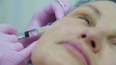 Kozmetologlar pembe eldivenler verip yetişkin kadınlara anestezi yapıyorlar. Şırıngalı, makro görüşlü. Güzellik enjeksiyon prosedürü.