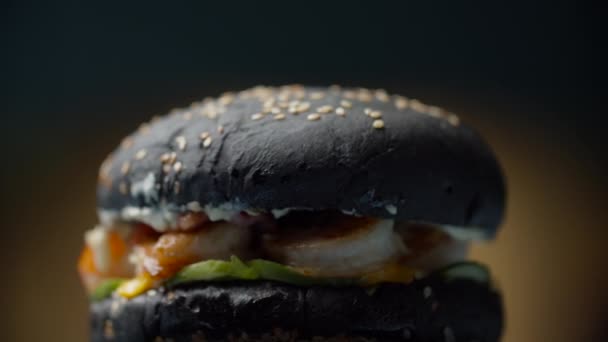 Lekkere zwarte zeevruchten hamburger met garnalen, gesmolten kaas, sla en groenten draaien op donkere achtergrond in slow motion. Burger met zwart broodje. — Stockvideo