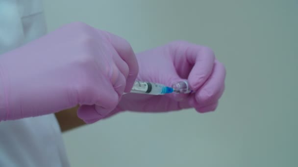 Cosmetologii pun mâna pe mănuși roz care preiau materiale cosmetice în seringă pentru injecția anti-îmbătrânire a umpluturii faciale. Procedura de injectare a frumuseții . — Videoclip de stoc