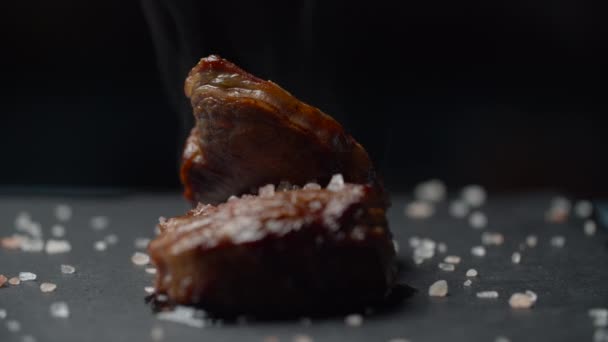 Närbild av nötkött biff roterande på svart bakgrund i slow motion. Kvinnlig hand sätta microgreen på filet mignon — Stockvideo