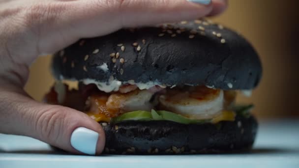 Mujer mano exprimiendo deliciosa hamburguesa de mariscos negros con camarones, queso derretido, lechuga y verduras en cámara lenta. Bollo de hamburguesa negra tomando su forma original después de la compresión . — Vídeo de stock