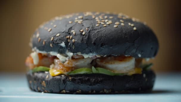 Vrouw hand wegnemen lekker zwart zeevruchten hamburger met garnalen, gesmolten kaas, sla en groenten in slow motion. — Stockvideo
