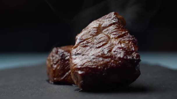 Close up of beef steak rotating on black background in slow motion. Two pieces of filet mignon with smoke. — Stock Video