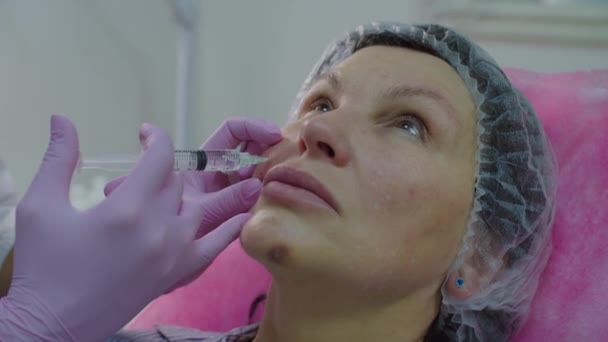 Kosmetolodzy w różowych rękawiczkach wykonujący wstrzyknięcie kosmetyczne przeciw starzeniu twarzy dorosłej kobiecie za pomocą strzykawki. Zabieg wstrzyknięcia urody w zwolnionym tempie. — Wideo stockowe