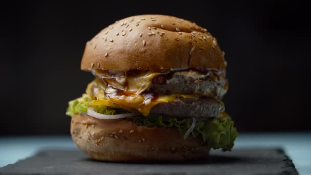 Vrouw hand nemen van lekker grote hamburger met dubbel rundvlees cutlet, gesmolten kaas, sla en groenten in slow motion. — Stockvideo