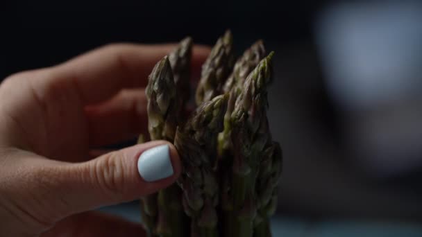 Vrouw hand vasthouden en aanraken van verse groene asperges bos, slow motion macro view. Close-up van groene aspergegroente in vrouwelijke handen. — Stockvideo