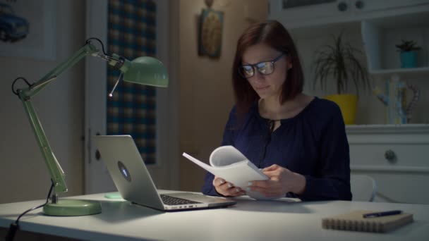 Unga 30-åringar arbetar från hemmet affärskvinna tittar igenom pappersdokument och bärbar dator. Ung kvinnlig vuxen entreprenör blad genom dokument hemma. — Stockvideo