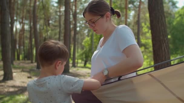 Twee jongens helpen twee moeders om een tent op te zetten in het bos voor hun lokale familie kampeertoerisme. Familie eco zomer toerisme. Langzame beweging, standvastig schot.. — Stockvideo