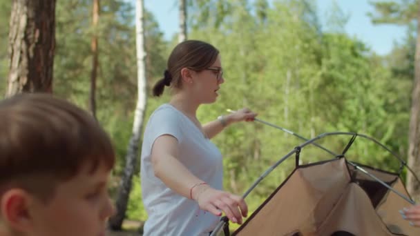 Two women and two boys having summer camping vacation in forest. Happy family of two mothers and two sons put up tent for camping. Slow motion, steadicam shot. — Stock Video