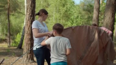 İki çocuk, iki anneye ormanda kamp yapmak için çadır kurmalarında yardım ediyor. Aile ekonomisi yaz turizmi. Yavaş çekim, sabit çekim.. 