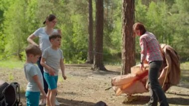 Mutlu çocuk neşeyle zıplıyor. İki kadın ve iki çocuk yaz kampında ormanda tatil yapıyorlar. İki anne ve iki oğulun ailesi kamp için çadır kurmuş. Yavaş çekim, sabit çekim..