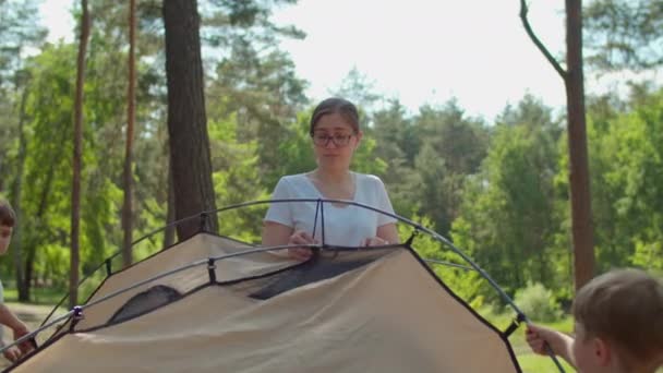 Two boys helping two moms to put up a tent in forest for their local family camping tourism. Family eco summer tourism. Slow motion, steadicam shot. — Stock Video