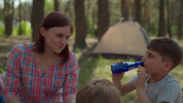 Deux mères et deux fils boivent des boissons froides au réfrigérateur sur une couverture de pique-nique pendant les vacances d'été en camping familial avec tente en forêt. Bonne famille avec chien Husky sibérien. Steadicam shot . — Video