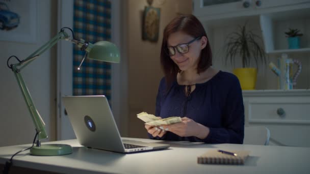 Treinta años trabajando desde casa mujer contando dólares dinero en efectivo y oliendo dinero. Joven mujer adulta con dinero en dólares pila en las manos en casa . — Vídeos de Stock