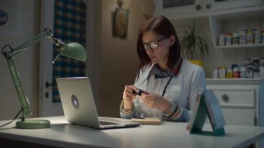 Evde çalışan 30 'lu yaşlardaki kadın doktor, çevrimiçi hastaya nabız oksimetresini nasıl kullanacağını gösteriyor. Boynunda steteskop olan beyaz doktor önlüklü kadın video görüşmesiyle konuşan hasta olacak..