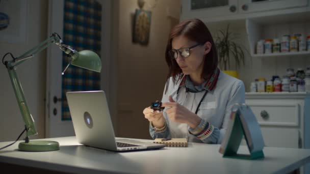 Working from home 30s female doctor shows online patient how to use pulse oximeter. Woman in white doctor coat with stethoscope on neck talking by video call with sick patient. — Stock Video