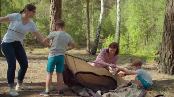 Två kvinnor och två pojkar som har sommarcampingsemester i skogen. Lycklig familj med två mödrar och två söner satte upp tält för camping. Slow motion, steadicam skott. — Stockvideo