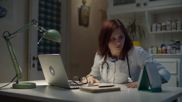 Jeune femme médecin trentaine dormant sur son lieu de travail. Femme endormie en manteau de médecin blanc avec stéthoscope sur le cou commence à travailler à l'aide d'un ordinateur portable et Internet. — Video