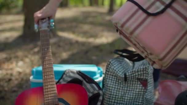 Dos madres jóvenes de 30 años con dos hijos colocando una manta rosa de picnic durante las vacaciones de campamento de verano con tienda en el bosque. cámara lenta, disparo steadicam . — Vídeos de Stock