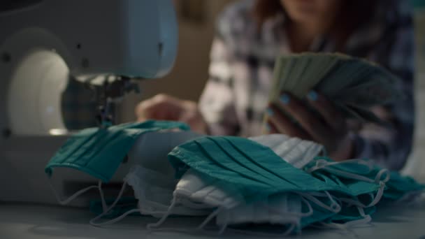 Primer plano de la mano de la mujer que cuenta dólares dinero para coser máscara protectora de la cara de trabajo desde casa. costurera femenina recibe dinero para la fabricación de mascarillas faciales . — Vídeo de stock