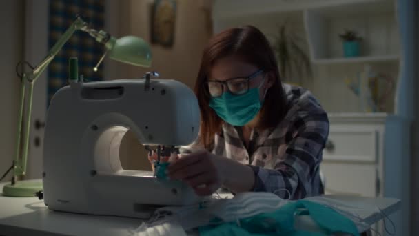 30s donna in maschera facciale cucire maschera protettiva facciale sulla macchina da cucire di lavoro a casa. Produzione di maschere per il viso a casa. — Video Stock