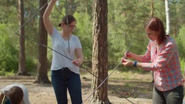 İki çocuk, iki anneye ormanda kamp yapmak için çadır kurmalarında yardım ediyor. Aile ekonomisi yaz turizmi. Yavaş çekim, sabit çekim.. 