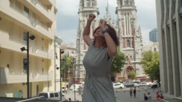 Energetische junge Frau, die Musik hört und auf einer Straße in der Stadt tanzt und mit den Händen winkt. Glückliche Stadttänzerin an sonnigem Tag. — Stockvideo