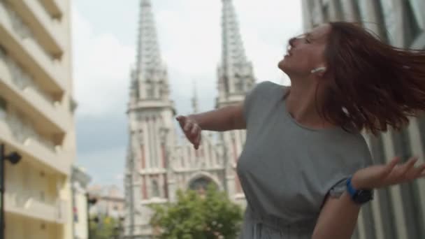 Energetische junge Frau, die Musik hört und auf einer Straße in der Stadt tanzt und mit den Händen winkt. Glückliche Stadttänzerin an sonnigem Tag. — Stockvideo