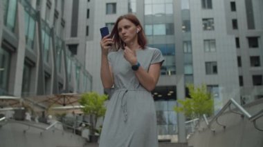 30 'lu yaşlardaki genç iş kadını şehir merkezindeki iş merkezinin yanında cep telefonuyla konuşuyor. Kadın yöneticinin dışarıda hücrede çevrimiçi konuşması var..