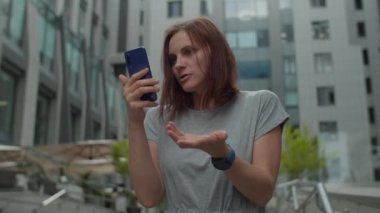 30 'lu yaşlardaki genç iş kadını şehir merkezindeki iş merkezinin yanında cep telefonuyla konuşuyor. Kadın yöneticinin dışarıda hücrede çevrimiçi konuşması var..