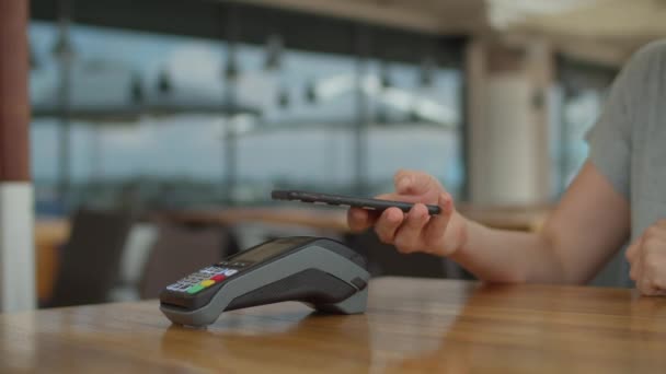 Ženská ruka platí účet s mobilním telefonem a bezkontaktní terminál zůstává na jídelním stole. Žena používající platbu NFC na svém mobilu.