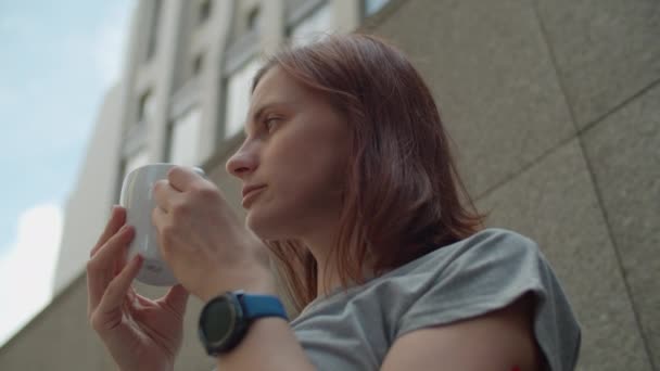 Jonge brunette uit de 30 die koffie drinkt in een café in de stad. Dame in draadloze oortelefoons geniet van het drinken van warme drank in het centrum. — Stockvideo