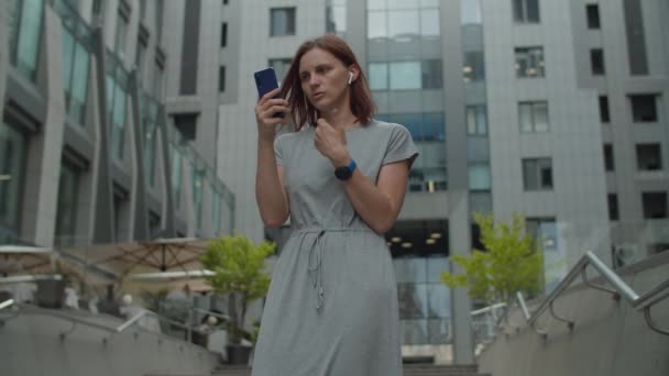 Jeune femme d'affaires trentenaire parlant par appel vidéo sur téléphone mobile debout près du centre d'affaires dans le centre-ville. Femme gestionnaire a conversation en ligne par cellule à l'extérieur. — Video