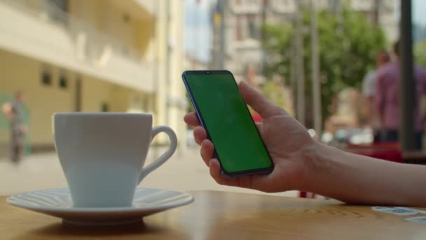 Samice ruční rolování mobilní telefon obrazovku s chromakey s šálkem kávy na stole. Žena dotýkající se zelený mobil obrazovka sedí ve městě kavárna. . 