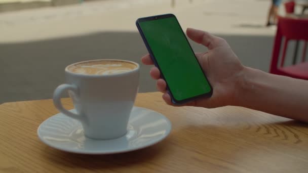 女性手滚动手机屏幕与铬钥匙与一杯咖啡放在桌上。坐在城市咖啡店里摸绿色手机屏幕的女人. . — 图库视频影像