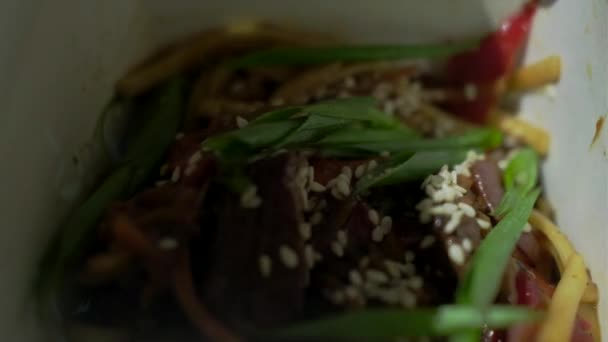 Close up of hand with chopsticks mixing noodle with meat and vegetables in paper box. Asian box food with chopsticks. — Stock Video