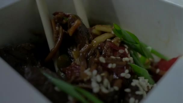 Zbliżenie strony z pałeczkami mieszając makaron z mięsem i warzywami w papierowym pudełku. azjatyckie pudełko żywności z pałeczek. — Wideo stockowe