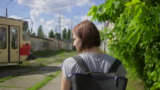 Jonge vrouwelijke volwassene wacht op het openbaar vervoer op het station. Stadstram rijdt de straat op. Vrouw kijkt naar stedelijke trein op straat. — Stockvideo