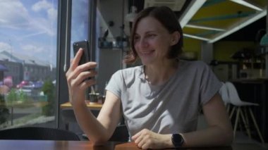 30 'lu yaşlardaki genç bir kadın cep telefonuyla konuşuyor ve gülümsüyor. Şehirdeki kafede oturan bir bayan cep telefonuyla konuşuyor..