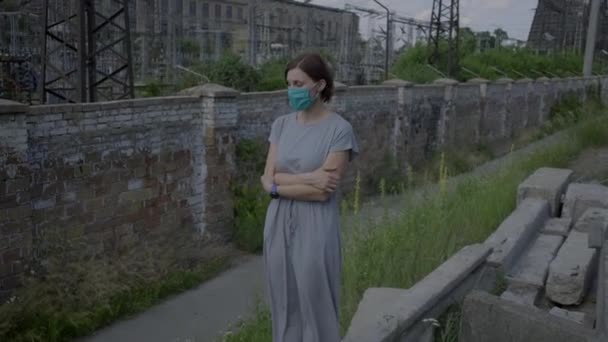 Giovane donna in maschera protettiva viso in piedi nel quartiere della città industriale nella giornata di sole. Donna in maschera da sola per strada. — Video Stock