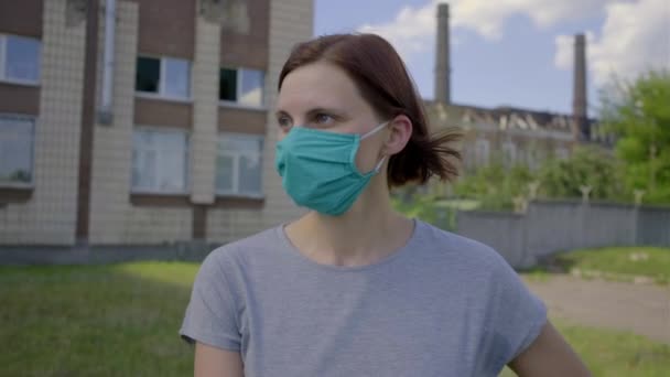 Junge Frau mit Gesichtsschutzmaske steht an einem sonnigen Tag im Industriegebiet. Frau mit Maske allein auf der Straße. — Stockvideo