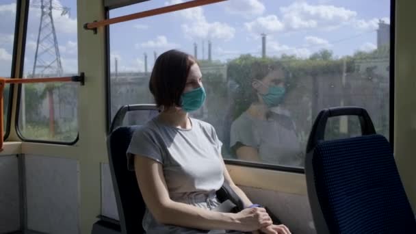 Mujer joven en máscara de protección facial cabalgando en transporte público. Mujer con máscara facial sentada junto a la ventana en un tren urbano vacío . — Vídeos de Stock