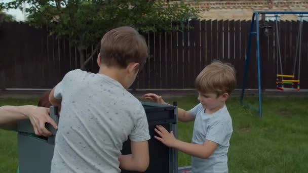 Dwóch braci pomaga młodej samotnej matce w montażu mebli z instrukcją na podwórku w słoneczny dzień. Wesołych rodzinnych zajęć na zewnątrz. Zwolnij, Steadicam shot. — Wideo stockowe
